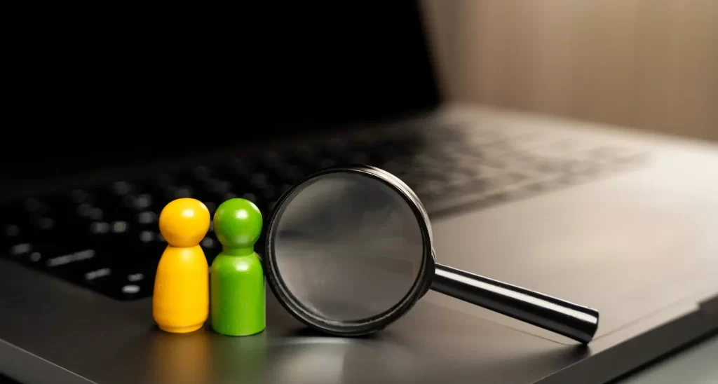 Peones de colores frente a lupa sobre teclado, representando análisis de audiencias en SEO.